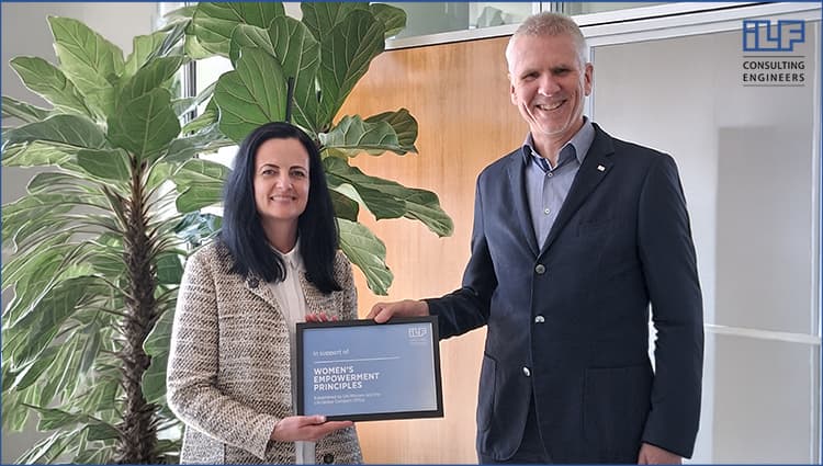 ILF Head of HR I. Stubenboeck and ILF CEO K. Laesser, standing indoors, holding a framed certificate supporting the Women’s Empowerment Principles, with large green plants in the background and an ILF Consulting Engineers logo visible in the corner.