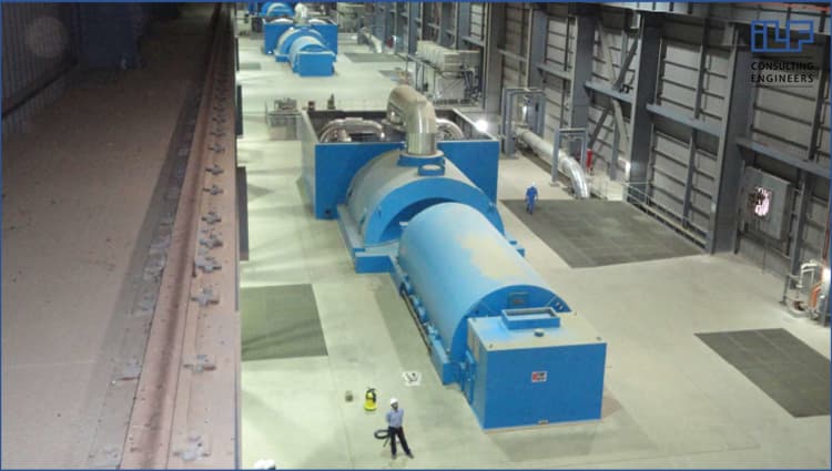 Large blue industrial turbines inside a spacious facility, part of a power generation or energy plant.